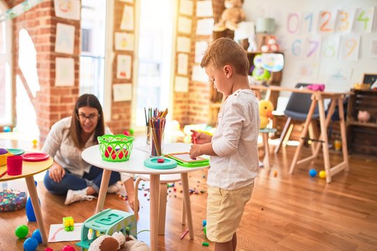 Beautiful teacher and toddler drawing using digital board around lots of toys at kindergarten