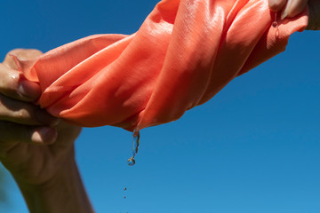 Hands twist pink cloth against blue sky.