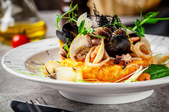 Italian food concept. Risotto with seafood, mussels, octopuses, squid. Serving dishes in a white plate. Modern serving in a restaurant. Background image. Copy space.