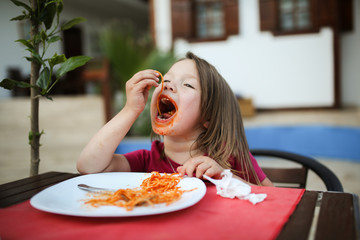 dirty girl child eating pasta with tomato sauce