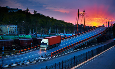 truck with container rides over the bridge, beautiful sunset, freight cars in industrial seaport,...