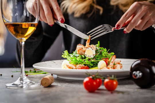 Girl in a restaurant eating Caesar salad with seafood and shrimp. A glass of white wine on the table. Modern serve in a restaurant. Background image. Copy space