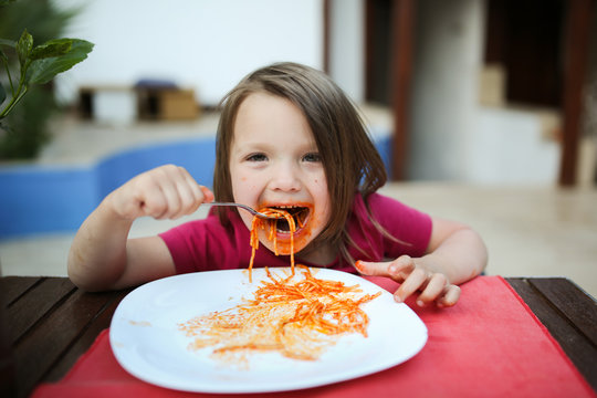 dirty girl child eating pasta with tomato sauce