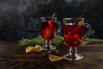 Two glass cups with mulled wine, with slices of orange and a stick of cinnamon are on a wooden...
