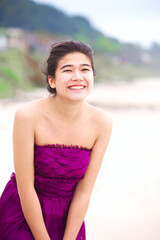 Happy, smiling teen girl in purple dress  laughing on beach