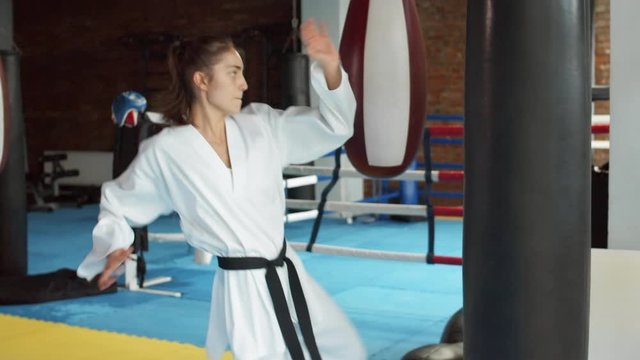 Medium shot of young pretty female fighter practicing kicks using punching bag inside boxing ring