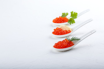 Red caviar in ceramic spoons on white background. Close-up, copy space.