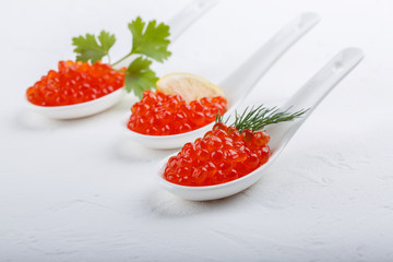 Red caviar in ceramic spoons on white background. Close-up, copy space.