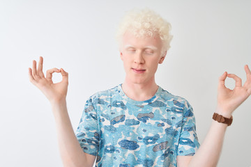 Young albino blond man wearing casual t-shirt standing over isolated white background relax and smiling with eyes closed doing meditation gesture with fingers. Yoga concept.