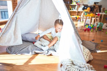 Beautiful blonde toddler sitting on the floor over blanket inside tipi at kindergarten