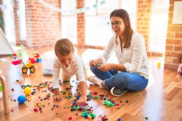 Beautiful teacher and toddler playing with building blocks around lots of toys at kindergarten