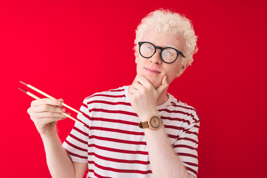 Young albino blond man holding chopsticks standing over isolated white background serious face thinking about question, very confused idea