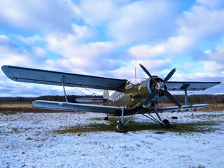 Green old piston aircraft biplane on the background of a winter landscape with forest, snow, grass and blue sky © Александр Боев