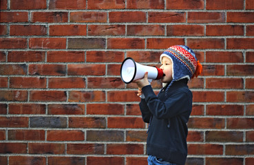 A boy holds a megafone in his hand and stands in front of the brick wall
