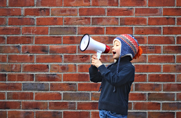 A boy holds a megafone in his hand and stands in front of the brick wall