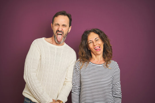 Beautiful middle age couple wearing winter sweater over isolated purple background sticking tongue out happy with funny expression. Emotion concept.