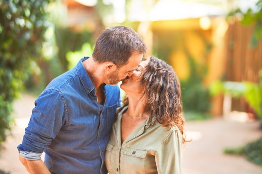 Middle age beautiful couple smiling happy and confident at town park. Standing with smile on face hugging and kissing