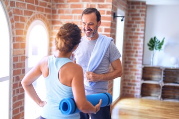 Middle age beautiful sporty couple smiling happy. Standing with smile on face holding mat and speaking at gym