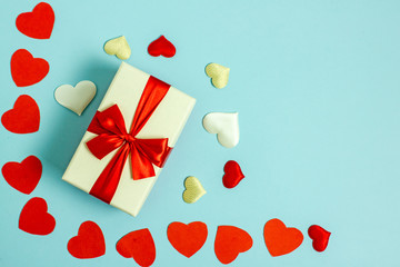  Valentine s day flatly copy space. On a blue background a gift box and a red bow, red paper hearts, hearts made of white fabric and red satin. In the center is a place for text.