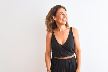 Middle age woman wearing black casual dress standing over isolated white background looking away to side with smile on face, natural expression. Laughing confident.