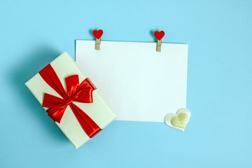 Valentines day flat lay copy space.  On a blue background is a white sheet of paper held by two rags decorated with red hearts. Near the leader in the box.Background for a declaration of love 