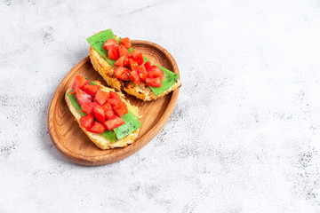 two Italian bruschettes with cheese and tomatoes on a wooden plate