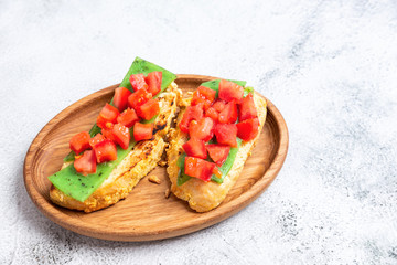 two Italian bruschettes with cheese and tomatoes on a wooden plate