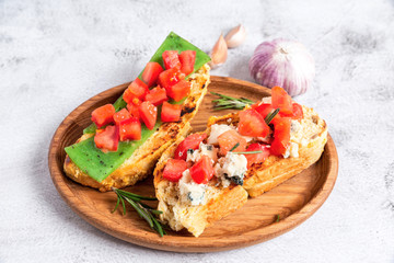 two Italian bruschettes with cheese and tomatoes on a wooden plate
