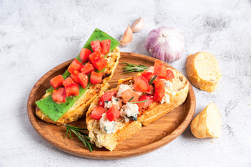 two Italian bruschettes with cheese and tomatoes on a wooden plate