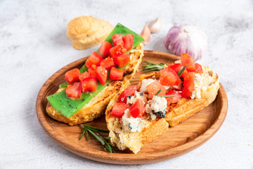 two Italian bruschettes with cheese and tomatoes on a wooden plate