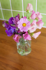 Mixed, fresh bunch of garden flowers in a jar on a kitchen table. Narrow depth of field with focus on Cosmos flower.