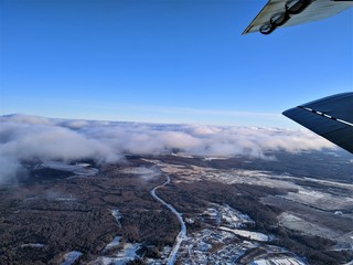 Aerial photography of winter landscape with clouds and blue sky with a biplane wing in the frame