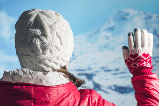 Back View Of Young Woman In A Winter Clothes And Christmas Gloves Waving Her Hand To Her Friends From Group Of Touristswhile Walking In The Snowy Mountains.