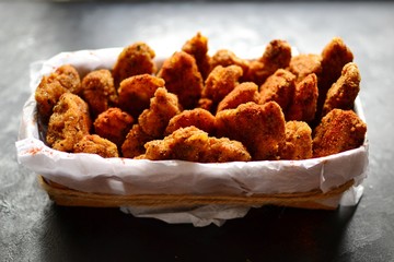Chicken nuggets on a dark background. Grilled fish and meat in batter. Fish sticks. Meat sticks. Nuggets with tomato and parsley in a basket. Place for your text.
