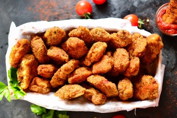 Chicken nuggets on a dark background. Grilled fish and meat in batter. Fish sticks. Meat sticks. Nuggets with tomato and parsley in a basket. Place for your text. Top view