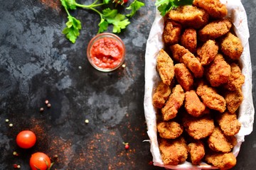 Chicken nuggets on a dark background. Grilled fish and meat in batter. Fish sticks. Meat sticks. Nuggets with tomato and parsley in a basket. Place for your text. Top view