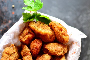 Chicken nuggets on a dark background. Grilled fish and meat in batter. Fish sticks. Meat sticks. Nuggets with tomato and parsley in a basket. Place for your text.