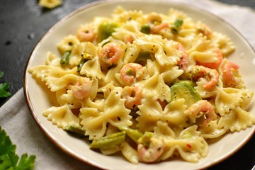 Italian pasta in a creamy sauce with shrimp on a plate, top view. Pasta in the form of bows on a dark table background. 