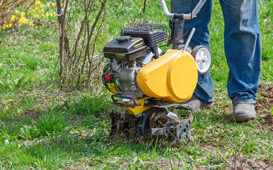 Obraz premium Cultivator for tillage in the garden,motor cultivator. Man Farmer plows the land with a cultivator.