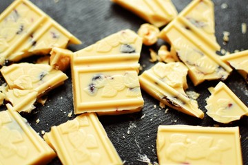 Broken bar of white chocolate. White chocolate with nuts on a dark background. Sweet food. Place for text