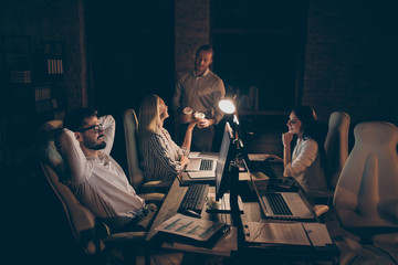 Photo of four business partners sitting chairs table working together late night little coffee break relaxation moment workaholics formalwear lamp light indoors