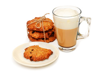 Transparent mug of coffee with milk, cappuccino or latte and homemade whole grain crispy oatmeal cookies with raisins. One cookie is bitten off. Concept of good start to the day. Closeup. Copy space