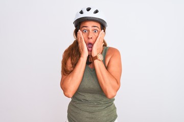 Middle age mature cyclist woman wearing safety helmet over isolated background afraid and shocked, surprise and amazed expression with hands on face
