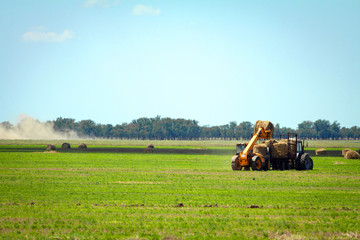 Tractor loading hay bales on truck agricultural works