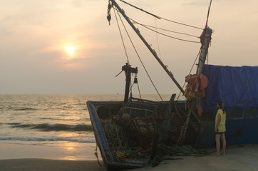 A woman in standing in front of a wooden fishing boat shipwreck enjoying the scenic sunset on colva beach india goa.