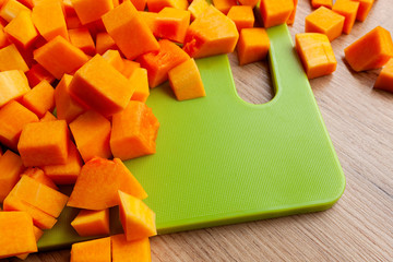 Vibrant, bright orange butternut squash, cut in cubes on green cutting board