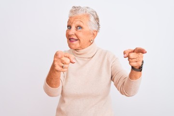 Senior grey-haired woman wearing turtleneck sweater standing over isolated white background pointing fingers to camera with happy and funny face. Good energy and vibes.