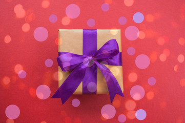 Giftbox tied with purple color ribbon on dark red background with beautiful confetti. Flat lay style.