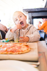Beautiful toddler child girl sitting on baby highchair drinking juice using straw with happy face