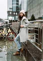 Young brunette woman walking around the city. She's wearing a gray coat and blue jeans